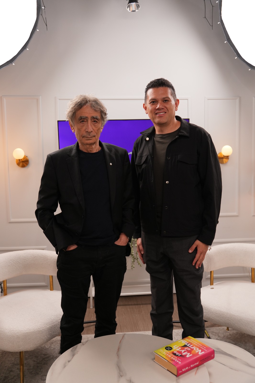 Oscar Rivas junto a Gabor Maté en un estudio de grabación, con el libro The Myth of Normal sobre la mesa