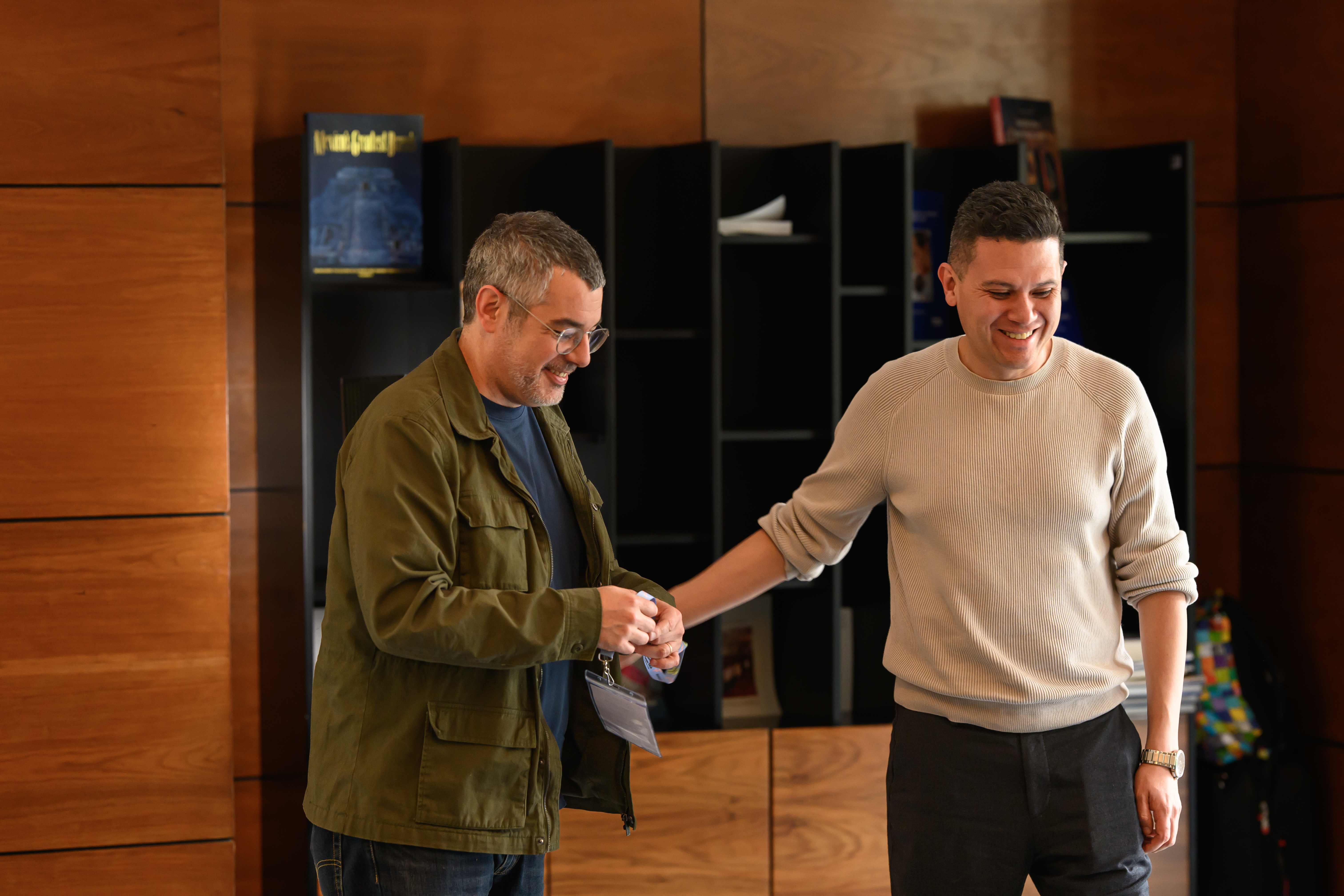 Oscar Rivas riendo junto al Dr. Nicolás Rodríguez del Real frente a una estantería de libros