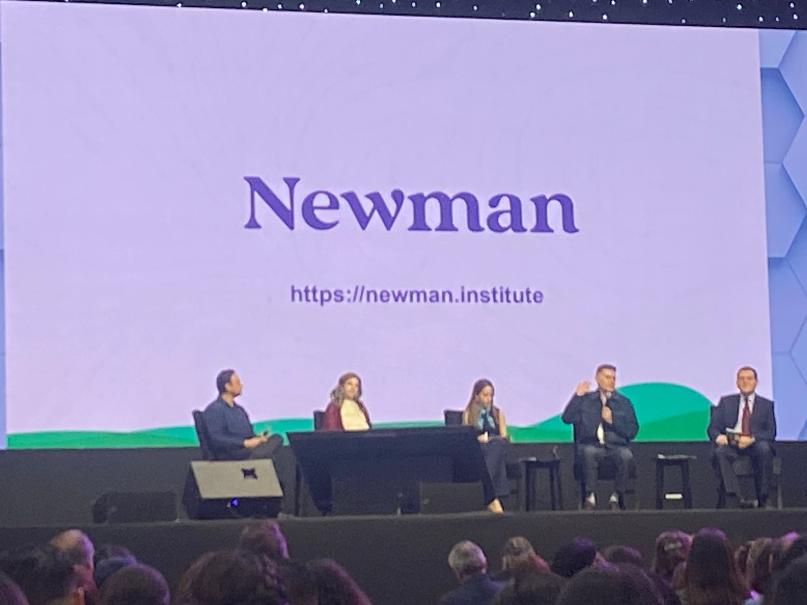 Panel de expertos sobre un escenario con el logo de Newman Institute proyectado en pantalla